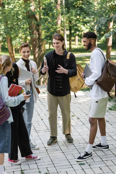Young multiethnic students with backpacks talking in summer park — Stock Photo