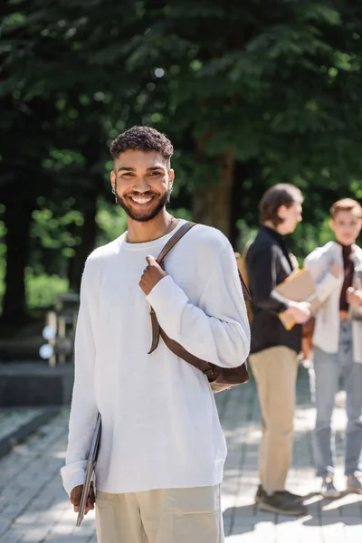 Positive african american student holding laptop and looking at camera in summer park — Photo de stock