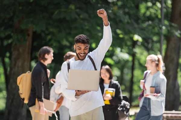 Emocionado estudiante afroamericano mostrando sí gesto y mirando el portátil en el parque - foto de stock