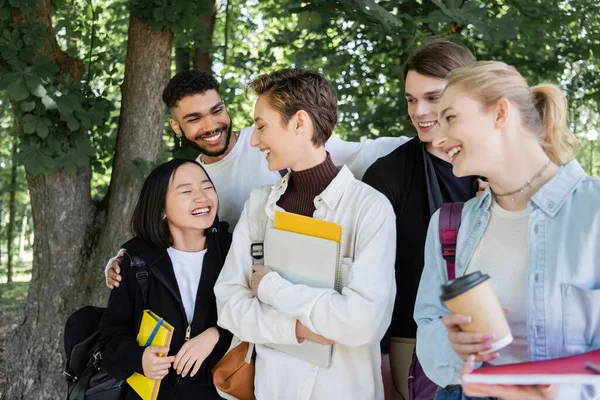 Estudantes multiculturais alegres com livros de cópia conversando no parque — Fotografia de Stock