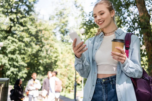 Lächelnder Student mit Smartphone und Kaffee to go im Park — Stockfoto