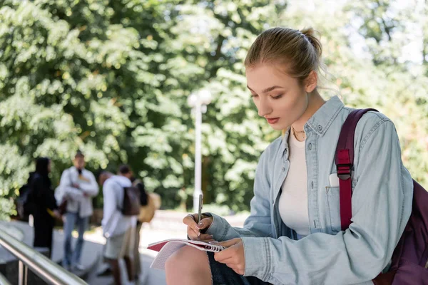 Student with backpack writing on notebook in park — Photo de stock