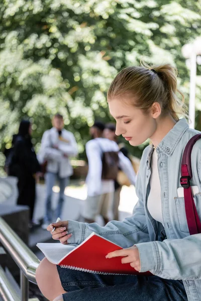 Side view of student holding pen and copy book in park — Stock Photo