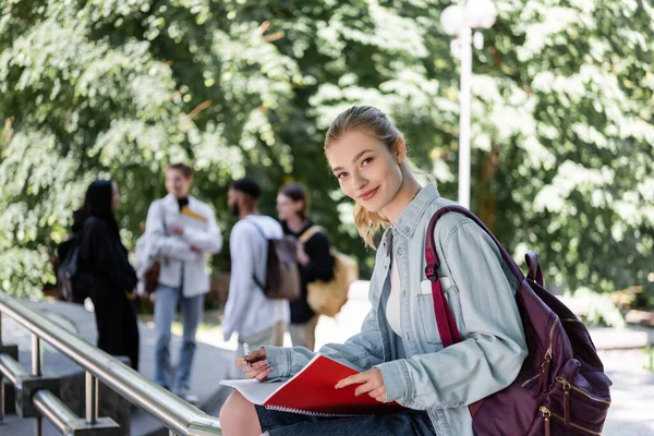 Studente positivo guardando la fotocamera mentre tiene il notebook nel parco — Foto stock
