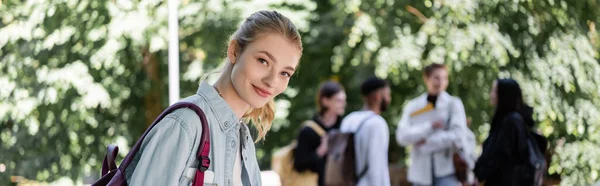 Estudiante alegre con mochila mirando a la cámara en el parque de verano, pancarta - foto de stock