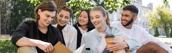 Positive multiethnic students looking at friend with copy book in park, banner — Stockfoto
