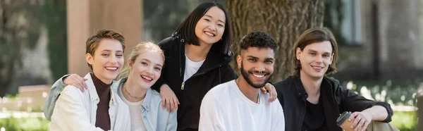 Молодые мультикультурные студенты смотрят на камеру в парке, баннер — стоковое фото