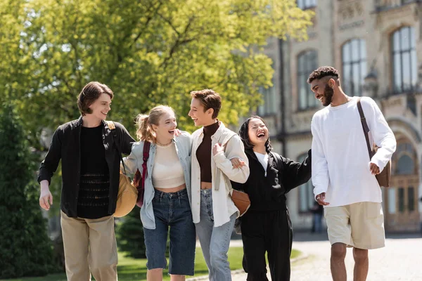 Веселі мультикультурні студенти з рюкзаками, що прокидаються біля університету в парку — стокове фото