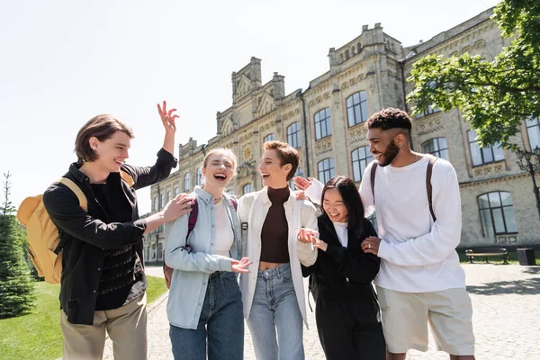 Cheerful student with backpack gesturing near multicultural friends outdoors — Foto stock