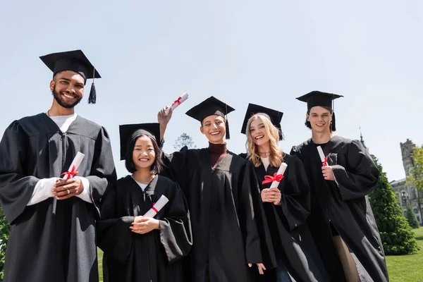 Multicultural bachelors holding diplomas outdoors — Foto stock