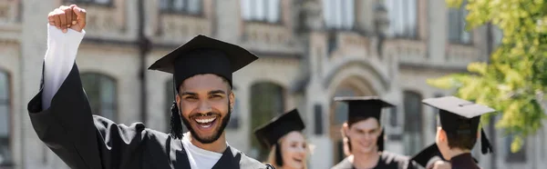 Excited african american bachelor in cap showing yes gesture in park, banner — Stock Photo