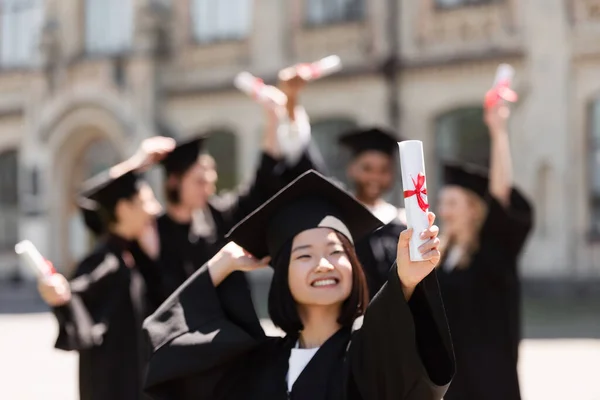 Heureux asiatique célibataire dans cap holding diplôme en plein air — Photo de stock