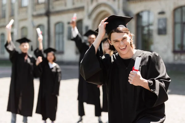 Baccalauréat souriant tenant chapeau et diplôme en plein air — Photo de stock