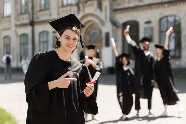 Бакалавр в капелюсі вказує на диплом на відкритому повітрі — Stock Photo