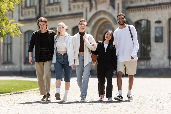 Jeunes étudiants multiethniques marchant et regardant la caméra près de l'université en plein air — Photo de stock