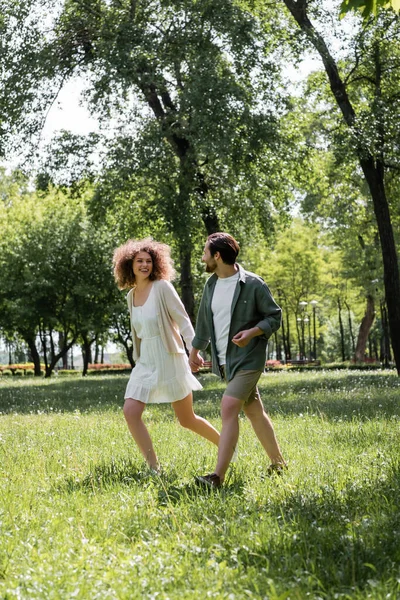 Повна довжина веселої молодої пари, яка зустрічається під час прогулянки в зеленому парку — стокове фото