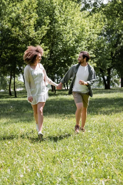 Full length of happy young couple holding hands and running during date in green park — Fotografia de Stock