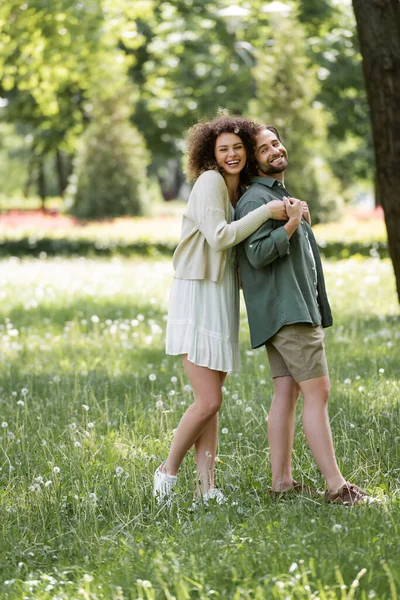 Full length of happy young couple having date and hugging in green park — Fotografia de Stock