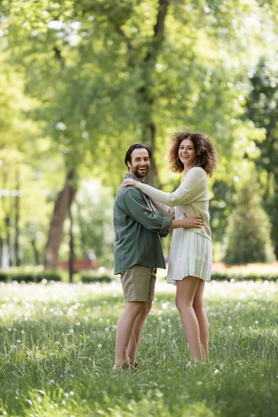 Full length of joyful young couple having date in green summer park — Stockfoto