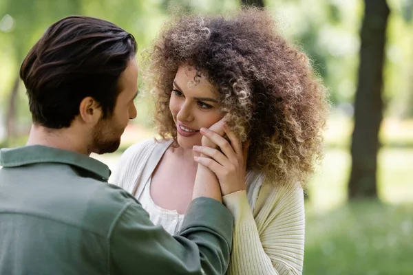 Tenero uomo toccante guancia di donna felice e riccia nel parco verde — Foto stock