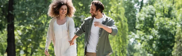 Gioiosa giovane coppia che si tiene per mano mentre cammina insieme nel parco estivo, striscione — Foto stock