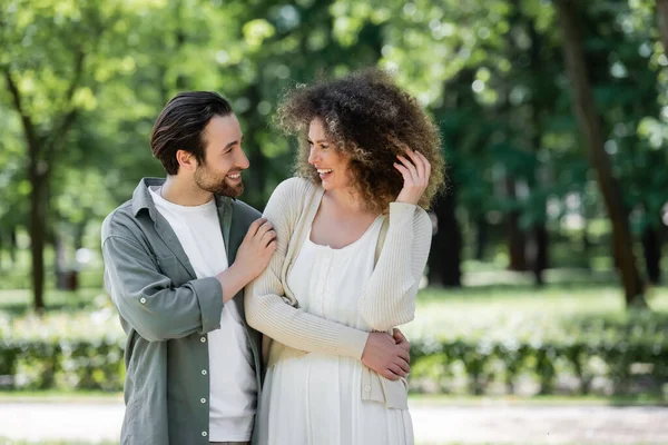 Alegre pareja joven sonriendo y mirándose en el parque de verano - foto de stock
