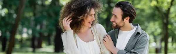 Alegre pareja joven sonriendo y mirándose en el parque de verano, pancarta - foto de stock