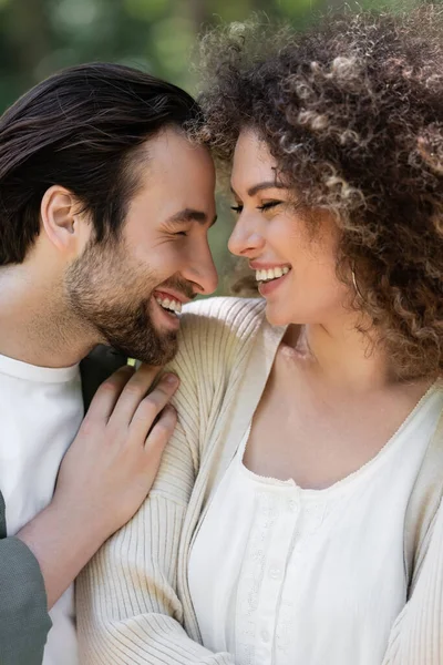 Joyeux jeune homme souriant avec femme heureuse et bouclée à l'extérieur — Photo de stock