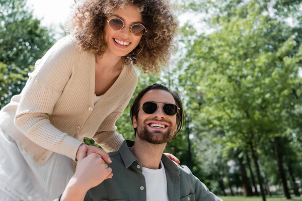 Zufriedener Mann und fröhlich gelockte Frau mit trendiger Sonnenbrille lächeln im Park — Stockfoto