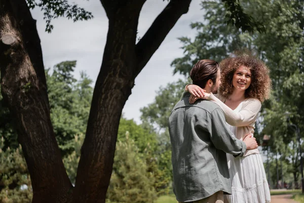 Glückliche lockige Frau umarmt bärtigen Mann bei Date im Sommerpark — Stockfoto