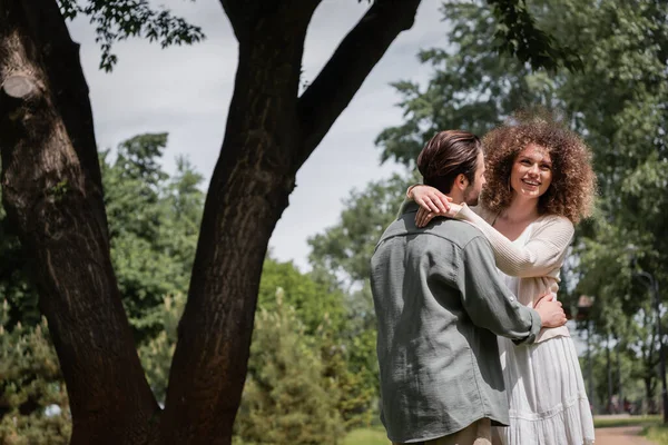 Happy curly woman hugging bearded man during date in summer park — Stock Photo