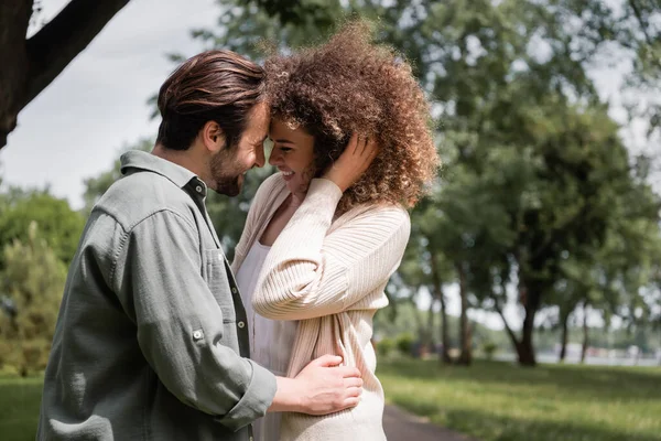 Happy curly woman hugging with bearded man during date in summer park — Stock Photo