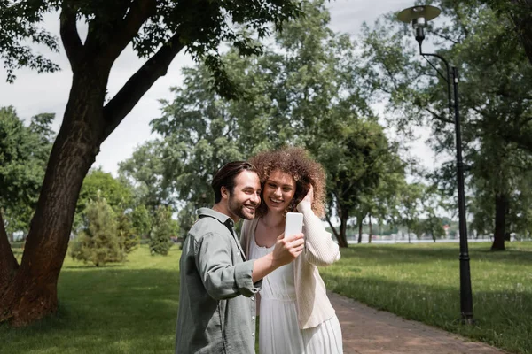 Jeune couple positif prenant selfie sur smartphone dans le parc d'été — Photo de stock