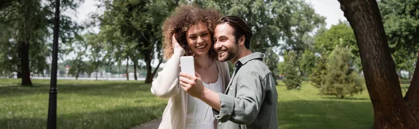 Positive young couple taking selfie on smartphone in summer park, banner — Stock Photo