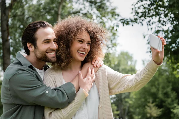 Positive young couple taking selfie on mobile phone in summer park — Stock Photo