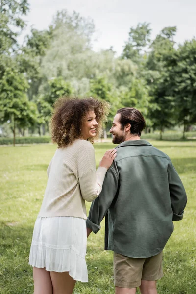 Curly woman in dress and man in summer clothes having date in park — Stock Photo