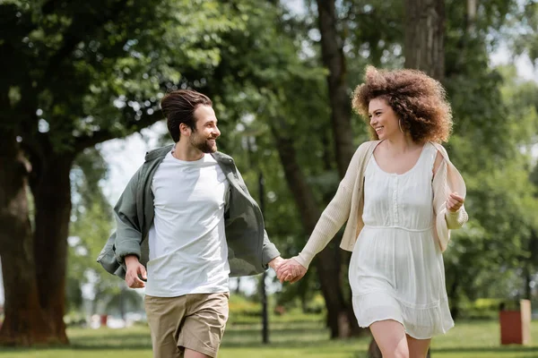 Heureux couple en vêtements d'été tenant la main dans le parc vert — Photo de stock