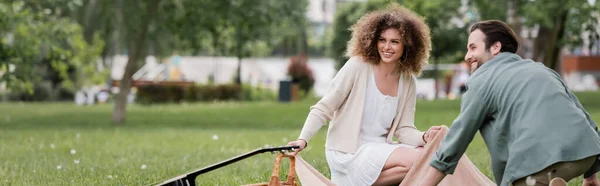 Feliz pareja sentada en manta cerca de picnic cesta de mimbre y guitarra acústica, pancarta - foto de stock