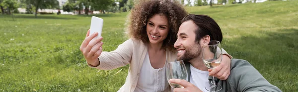 Happy young couple taking selfie on smartphone during summer picnic in park, banner — Photo de stock