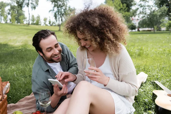 Happy young couple using smartphone during summer picnic in park — Stockfoto