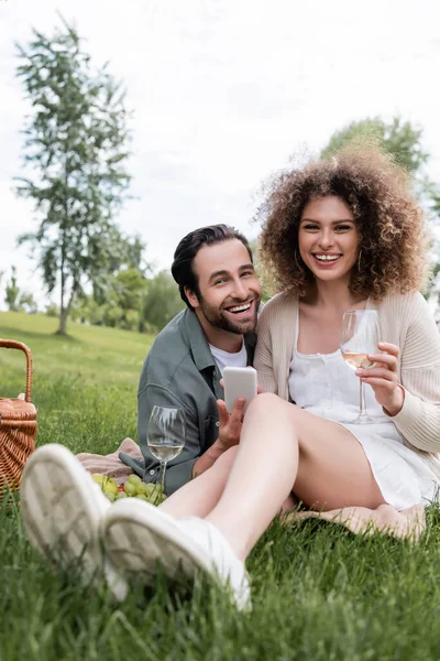 Happy young man and woman using smartphone during summer picnic in park — Photo de stock