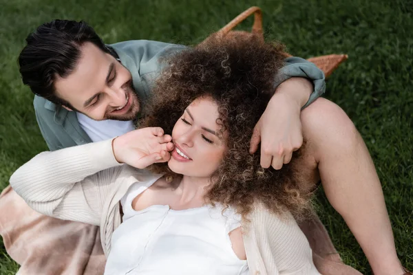 Top view of curly woman lying on happy boyfriend during picnic in summer park — Stockfoto