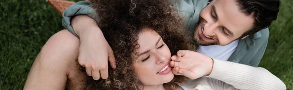 Top view of curly woman lying on happy boyfriend during picnic in summer park, banner - foto de stock