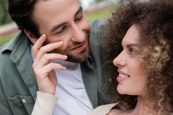 Retrato de mujer rizada sonriente coqueteando con novio feliz en verano - foto de stock