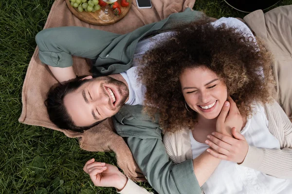 Top view of curly woman lying on joyful boyfriend during picnic in summer park — Stock Photo