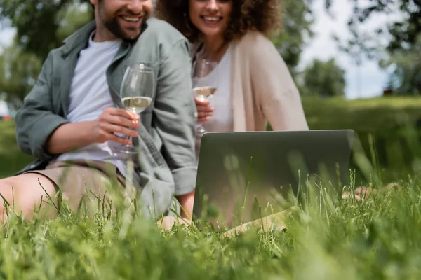 Vue recadrée de couple heureux tenant des verres de vin tout en regardant un film sur ordinateur portable à l'extérieur — Photo de stock