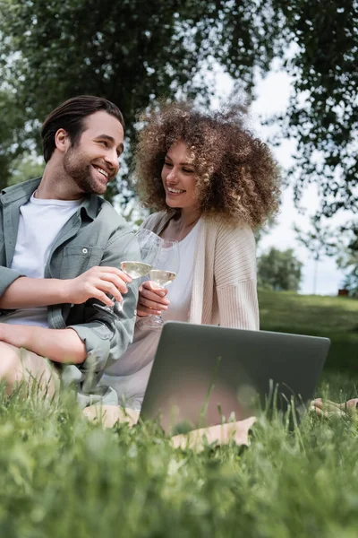 Glückliches Paar klimpert mit Weingläsern, während es draußen einen Film auf dem Laptop anschaut — Stockfoto