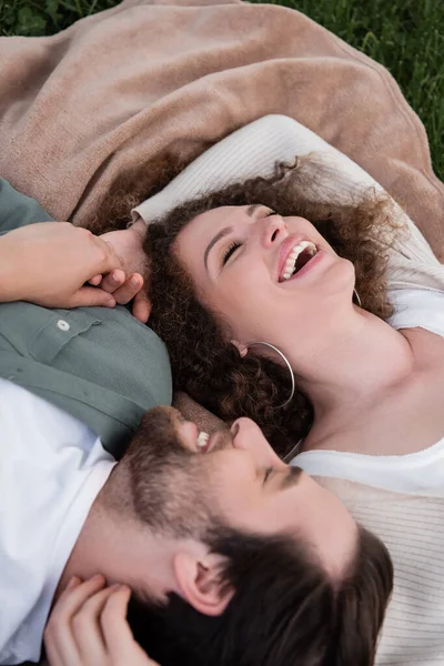 Top view of joyful young woman and man with closed eyes laughing while lying on soft blanket — Stock Photo