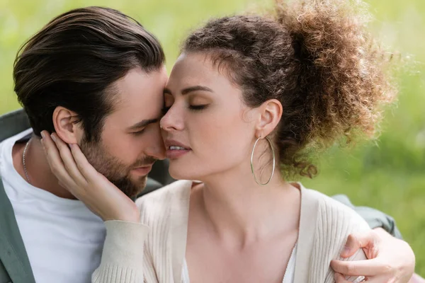 Femme tendre et bouclée touchant visage de l'homme barbu dans le parc — Photo de stock