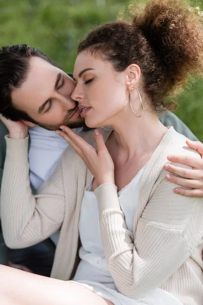 Hombre barbudo y mujer rizada abrazándose y besándose en el parque - foto de stock